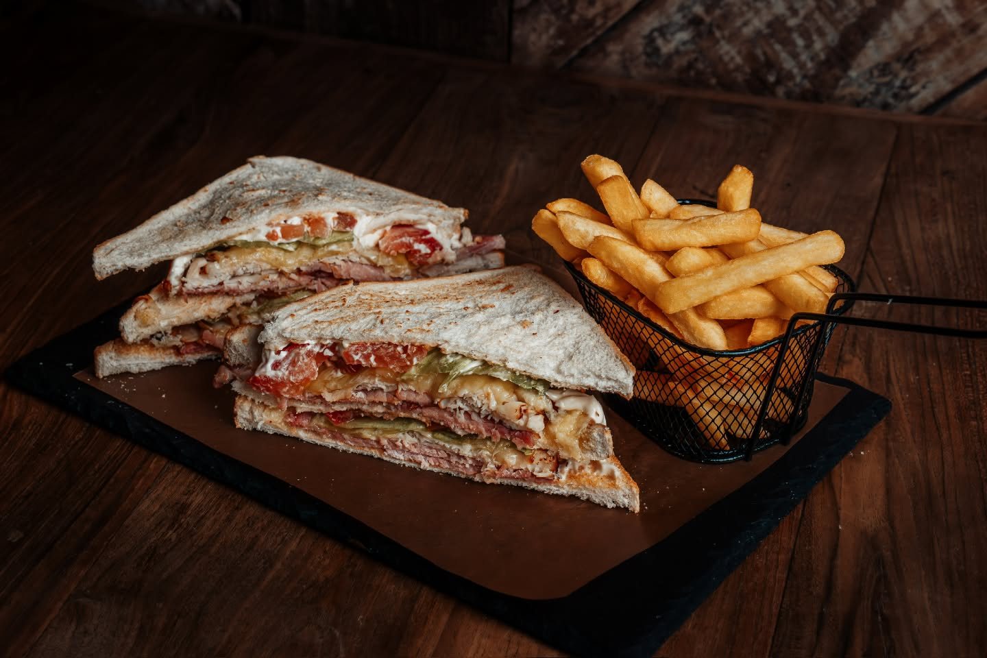A Clubhouse Sandwich with crisps on dark wood